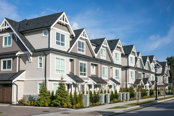 A row of townhouses in a residential neighborhood, showcasing FHA condo approval signage in front of one unit.  