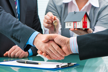 A home buyer and seller shake hands over a house model, discussing a seller concession deal.  