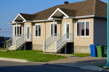 Multi-family home featuring a distinctive green roof surrounded by trees and a clear blue sky.  